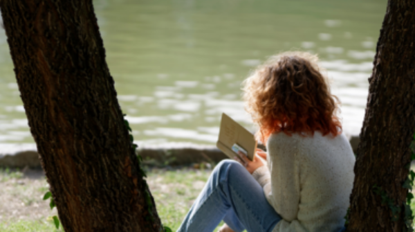 Meisje leest boek in hetpark onder een boom aan het water