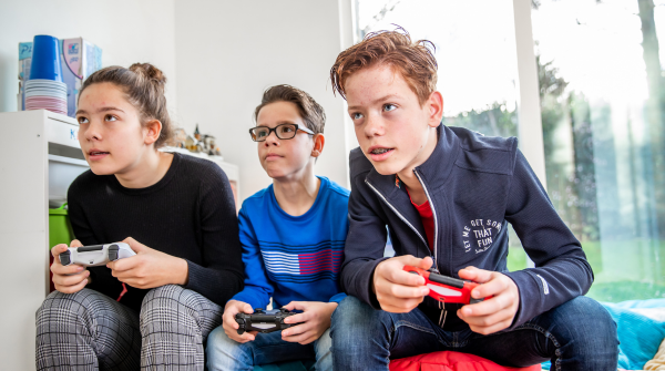 3 kinderen zittend op een bank met een game controler in hun hand,